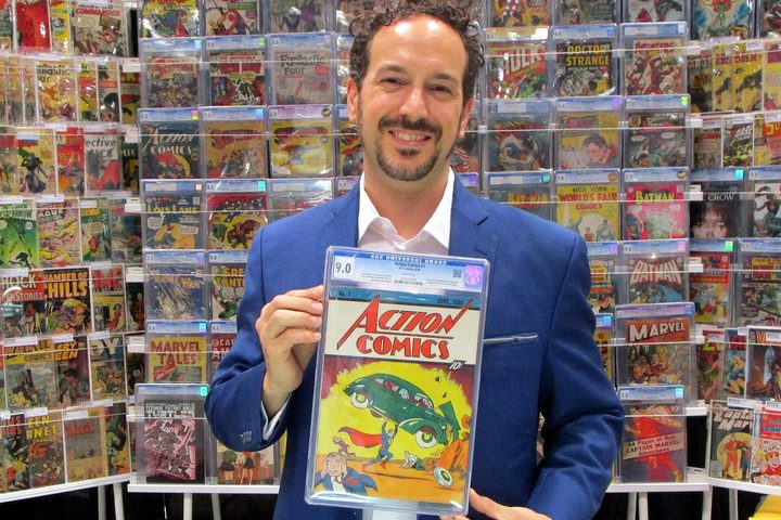 A dealer holding a graded copy of Action Comics No. 1 in front of a wall of comic books