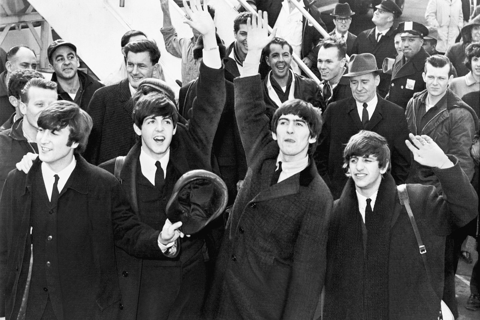 The Beatles waving to a crowd in a black-and-white press photograph from 1964