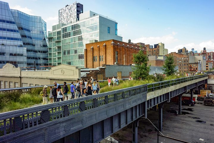 Visitors walking the planted deck of the High Line on its elevated steel viaduct above a Manhattan street
